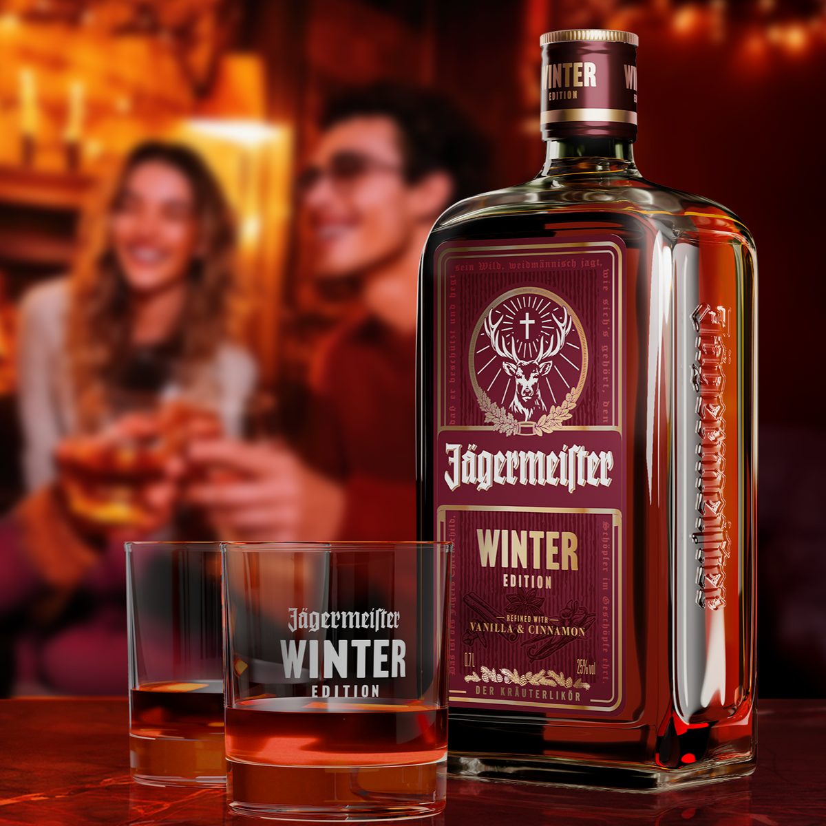 A bottle of Jagermeister Winter Edition  stands on a wooden table beside two matching etched glasses, with a blurred bar scene and two people in the background.