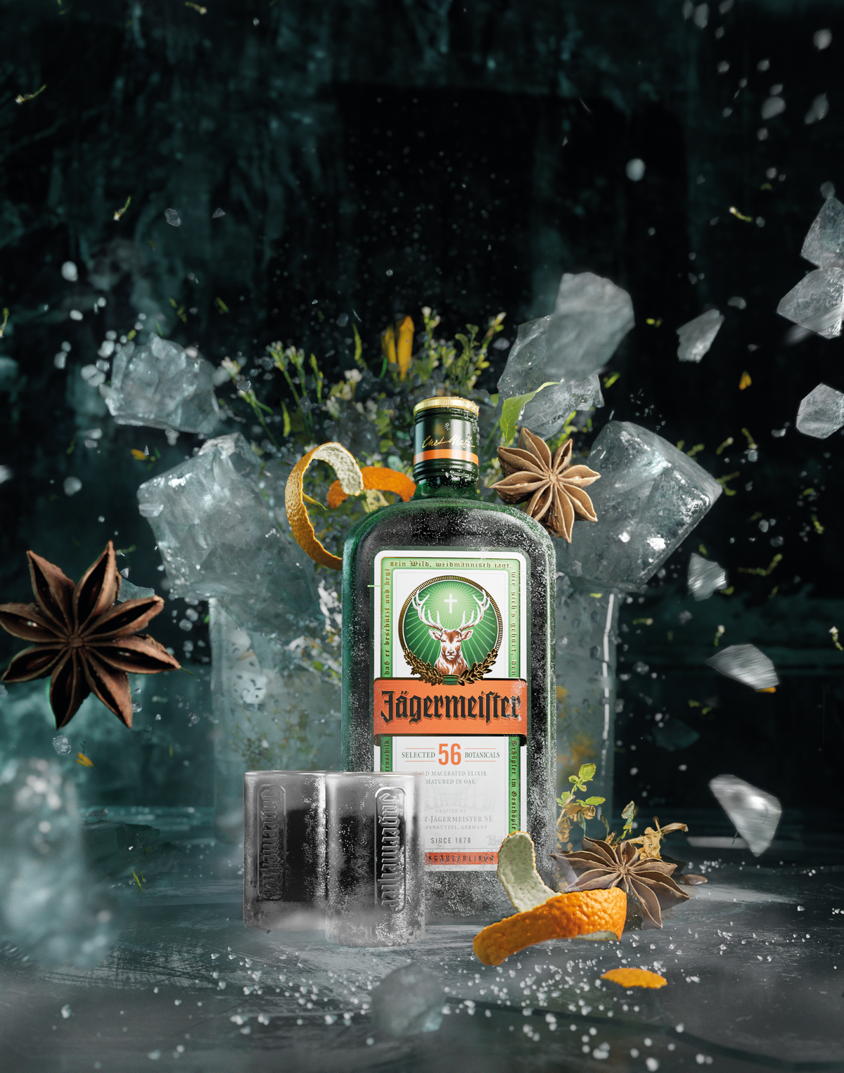 A bottle of Jägermeister 56-proof spirit stands in a dramatic studio setup with crushed ice, shattered glass, star anise, orange curls, and two filled tumblers. The background is dark and moody, with floating ice fragments and a reflective surface below.