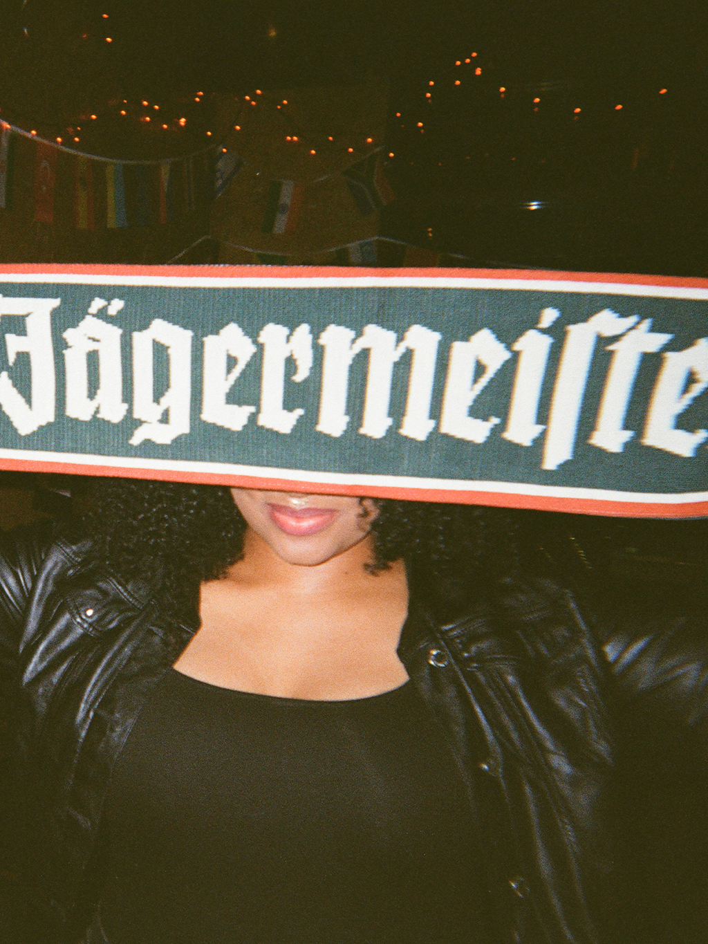Person holding a Jägermeister scarf in front of their face with a dark background.