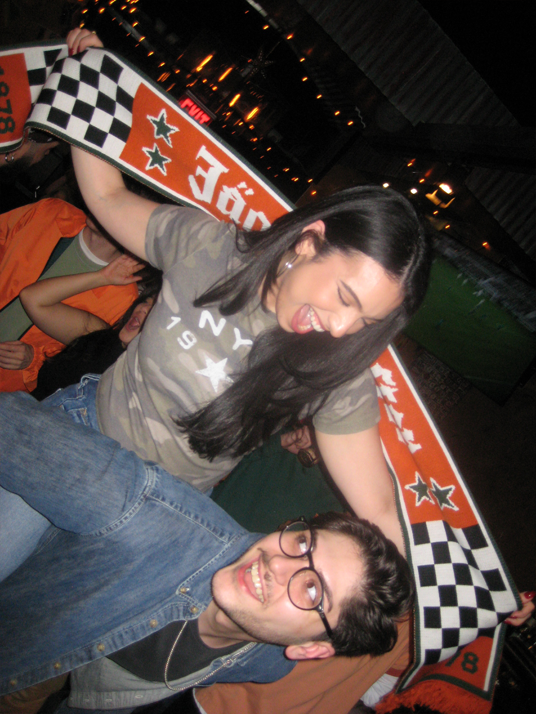 Two people posing with a large Jägermeister Racing scarf