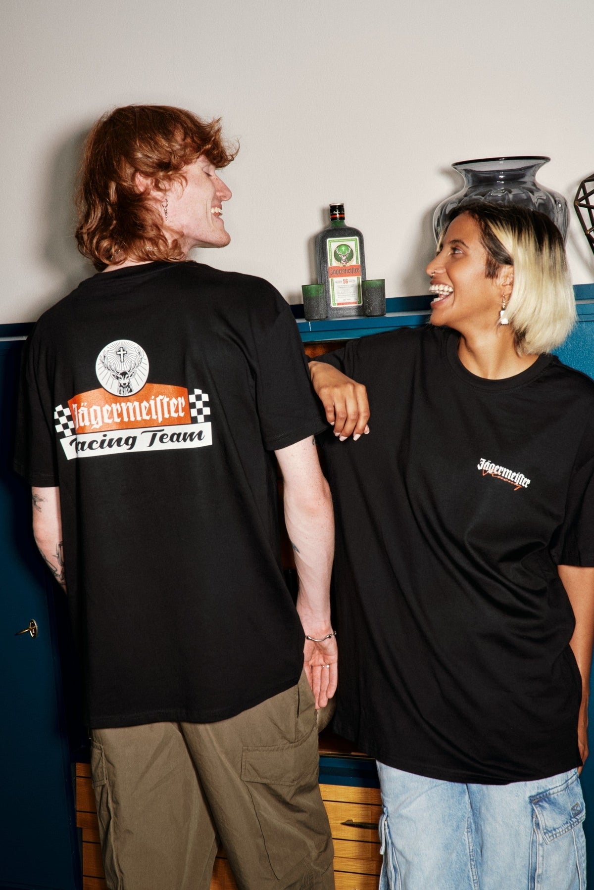 Twee mensen in zwarte Jägermeister-racing T-shirts met een logo en tekst, dicht bij elkaar staand.