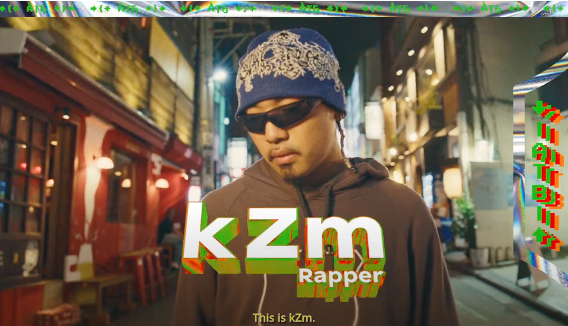 A man wearing a blue patterned beanie, black sunglasses, and a brown hoodie stands on a city street at night. Large text overlays read 'kzmr Rapper'.