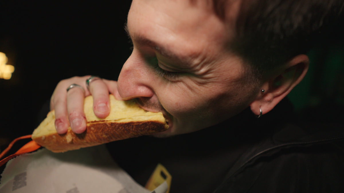 A close-up lifestyle shot of a man biting into a thick slice of toasted bread, set against a dark, moody background.