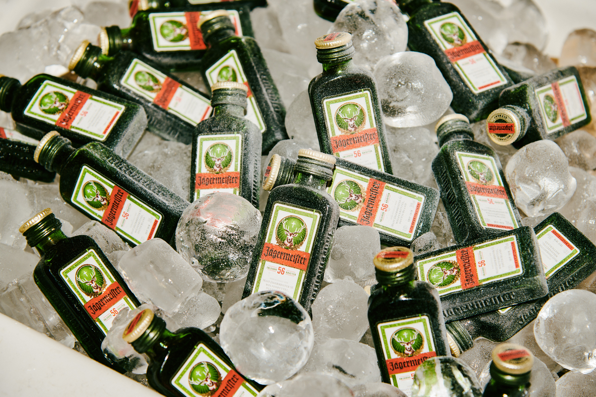 Multiple small Jägermeister bottles arranged in a bed of ice, showing the dark glass bottles, gold caps, and green-and-white labels.