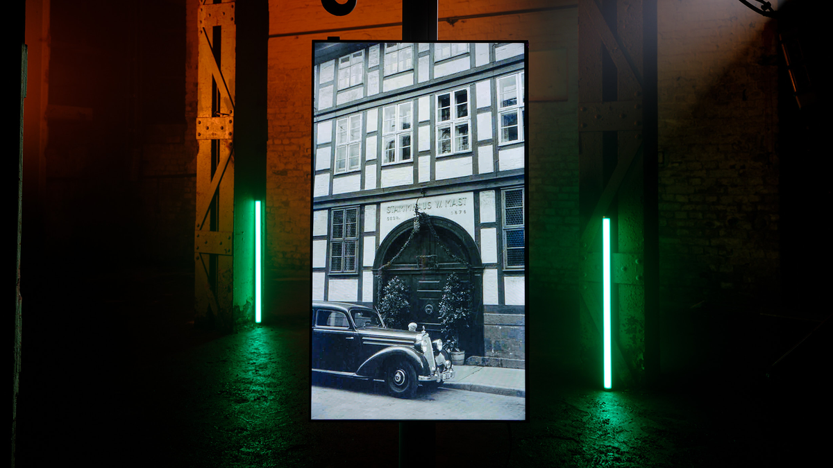 A vertical LED light box displaying a black and white photograph of a historic half-timbered building and a vintage car, set in a dark industrial space with green neon lights.
