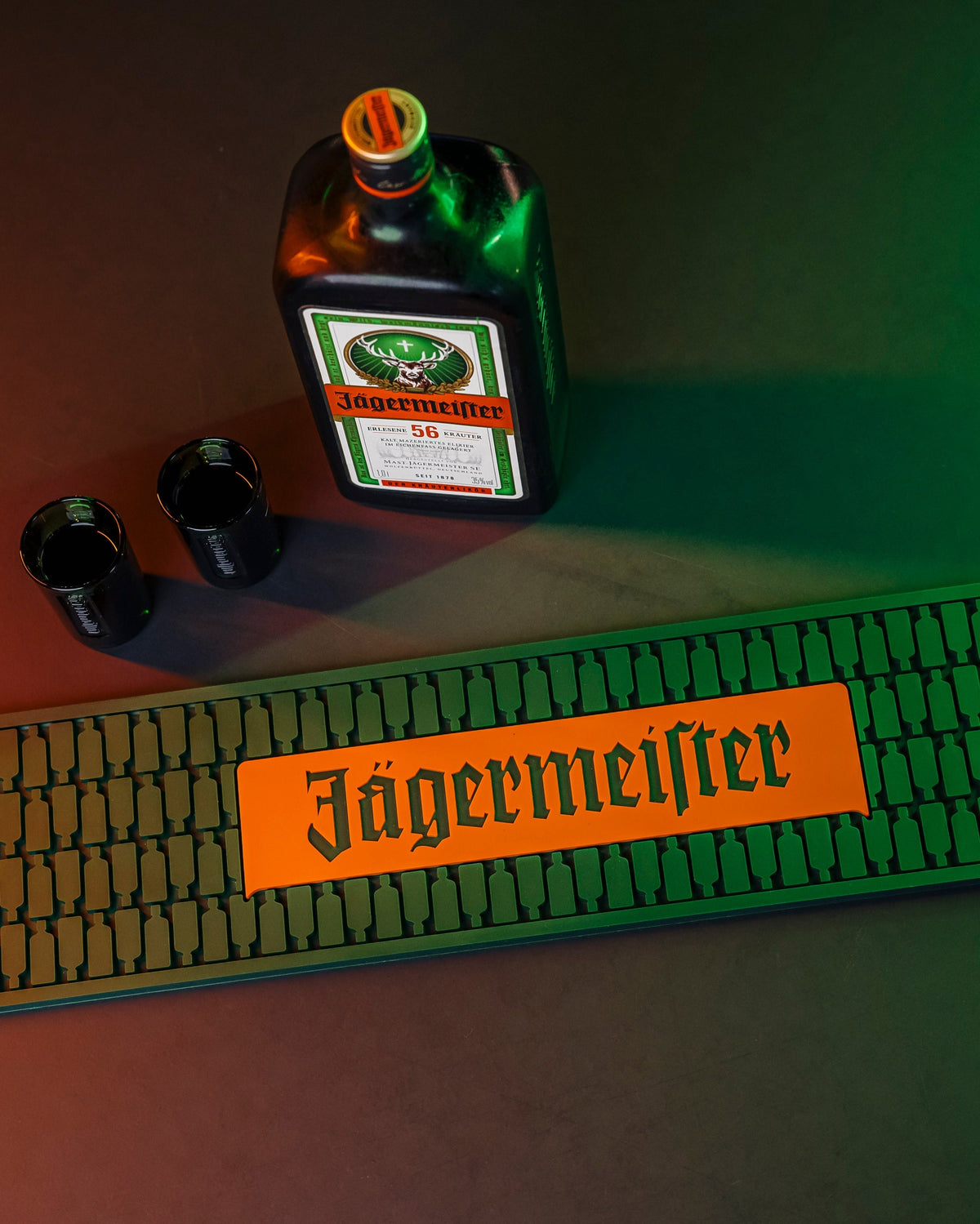 Jägermeifter bottle, two shot glasses and bar mat on a dark surface