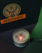 Jägermeister logo on a dark background with a small round device emitting light.