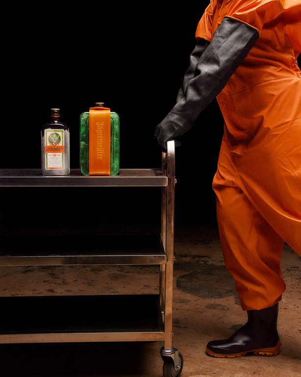 Person in orange jumpsuit with coldblock and Jägermeister bottle on a cart against a dark background