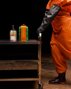 Person in orange jumpsuit with coldblock and Jägermeister bottle on a cart against a dark background