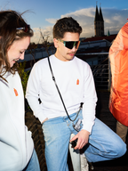 Two People wearing white Jägermeister sweatshirts and Jägermeister fast glasses on a rooftop terrace, with a church tower and city skyline in the background.