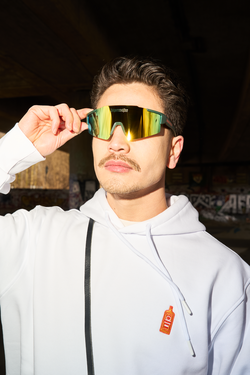 Person wearing reflective Jägermeister sunglasses and a white hoodie with a bottle logo.