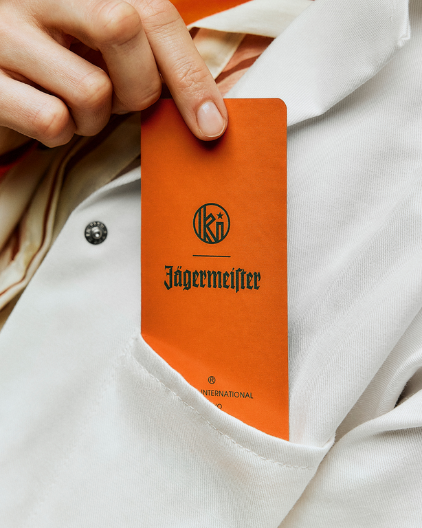 Jägermeister and Kuumba label on an orange fragrance paper held by a hand against a white coat background