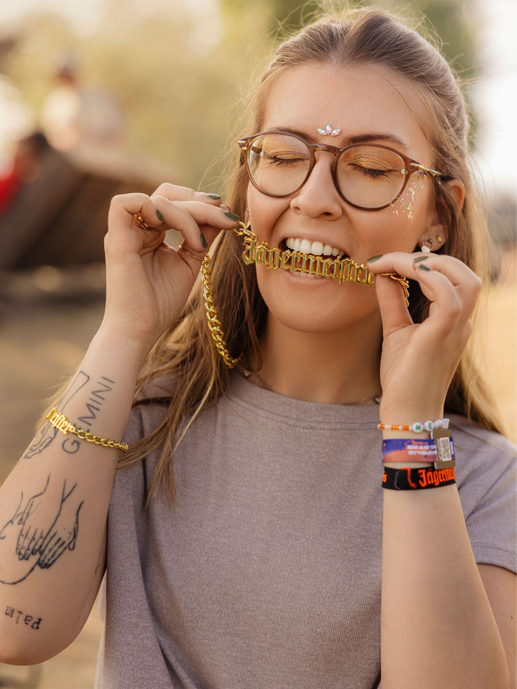 Woman wearing gold chain Jägermeister necklace and bracelets in a festival setting.