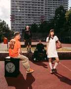 Group of people on an outdoor basketball court, featuring a person in a white Jägermeister polo dress holding a basketball, alongside others wearing Jägermeister apparel, with a high-rise building in the background.