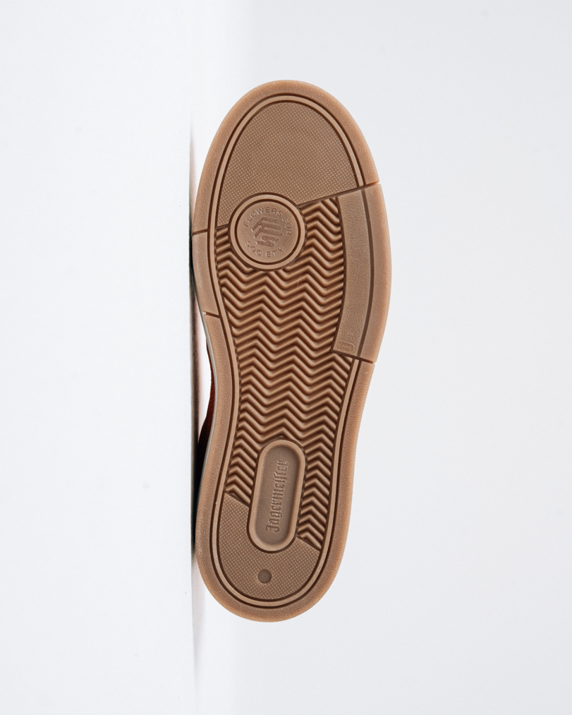 A top-down view of a brown rubber shoe sole, showing the tread pattern and the embossed logos of Jägermeister and Flowers for Society