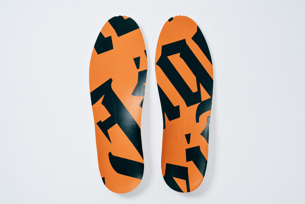 A pair of athletic shoe insoles with a Jägermeister orange and black pattern design, shown from a top-down view on a light background.