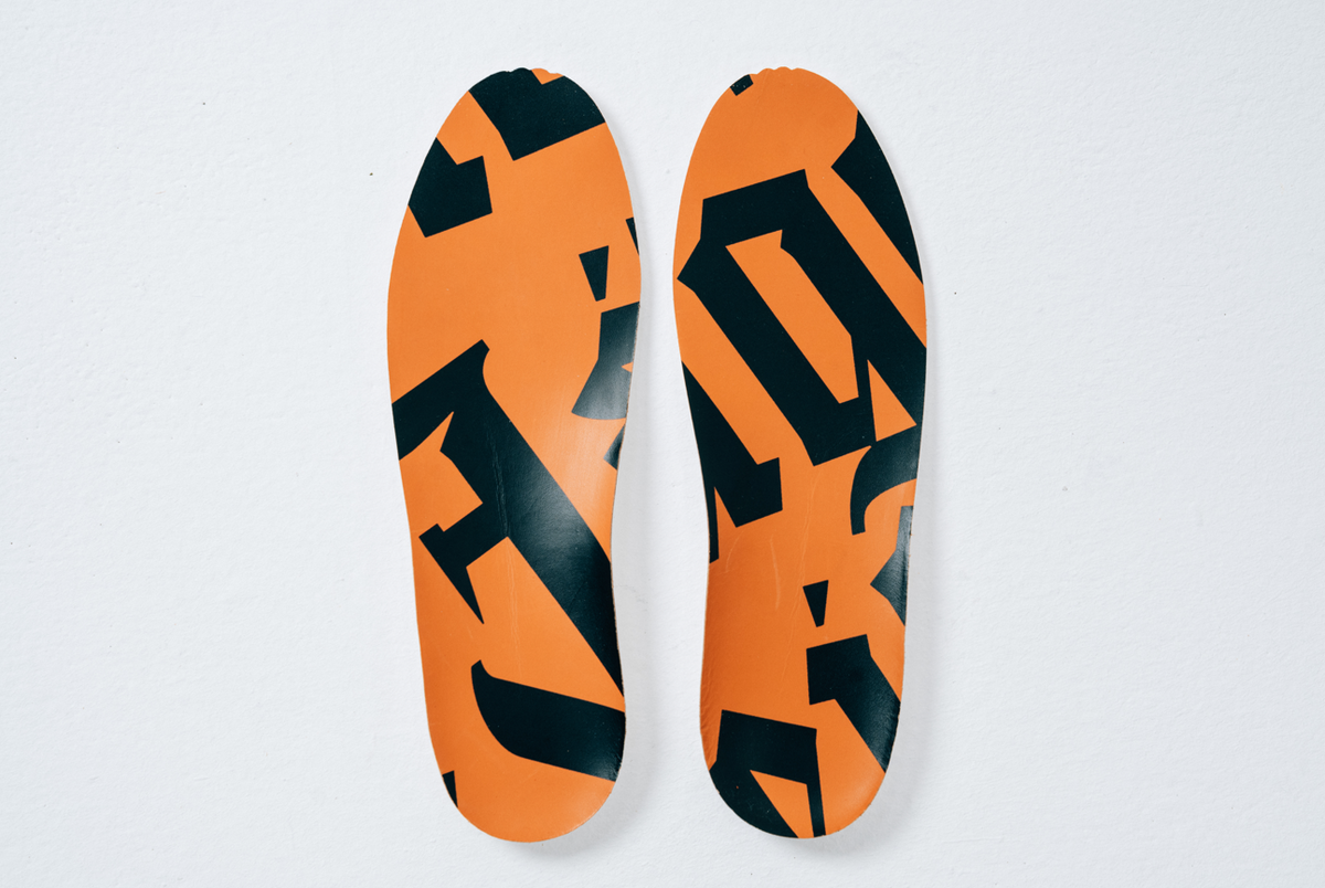 A pair of athletic shoe insoles with a Jägermeister orange and black pattern design, shown from a top-down view on a light background.
