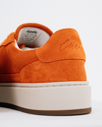 Close-up rear three-quarter view of an orange Jägermeister sneaker with a thick off-white platform sole and brown outsole, showing the heel tab with embroidered name 'Curt'