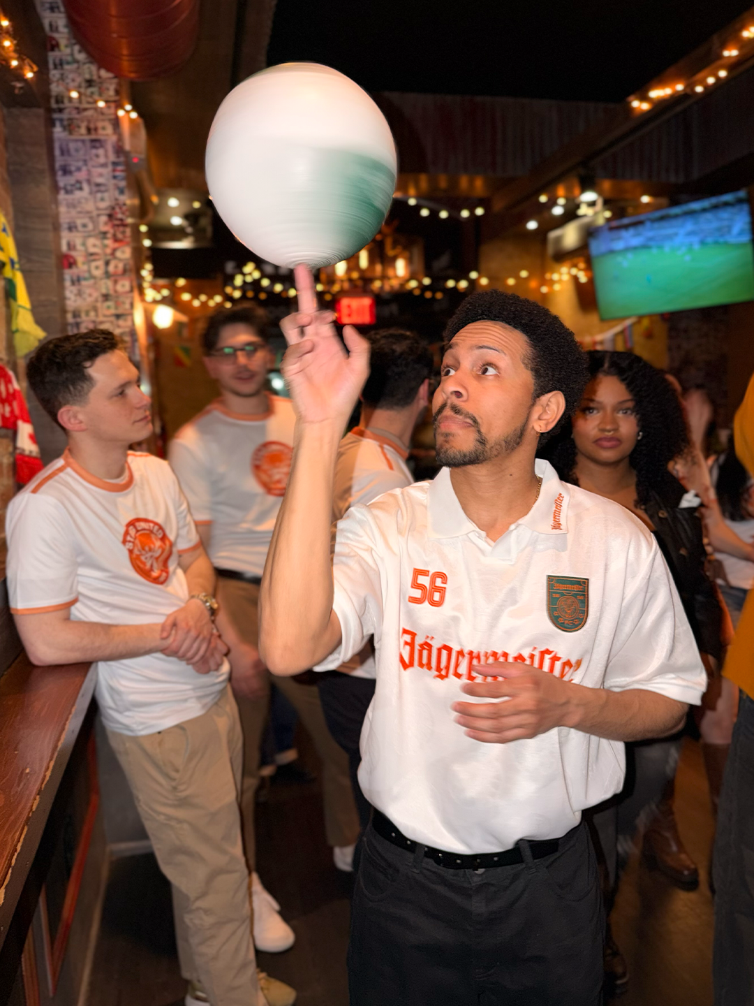Man holding a colorful ball in a bar setting with other people around